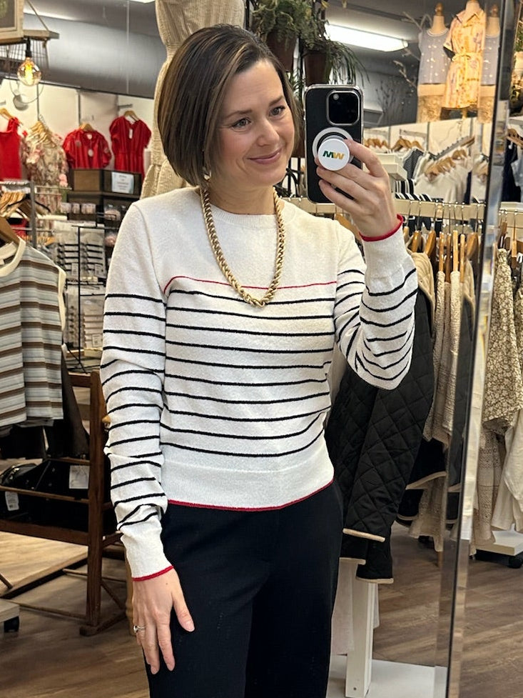 Woman taking a mirror selfie in a clothing store wearing a striped sweater and black pants.